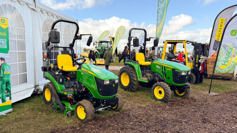 Tracteurs compacts John Deere verts et jaunes exposés sur le stand HAAG lors de la Foire de Poussay avec visiteurs et drapeaux