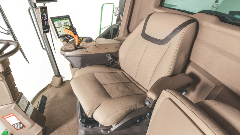 Siège conducteur ergonomique John Deere beige avec accoudoirs, réglages multiples et maintien lombaire dans une cabine de tracteur