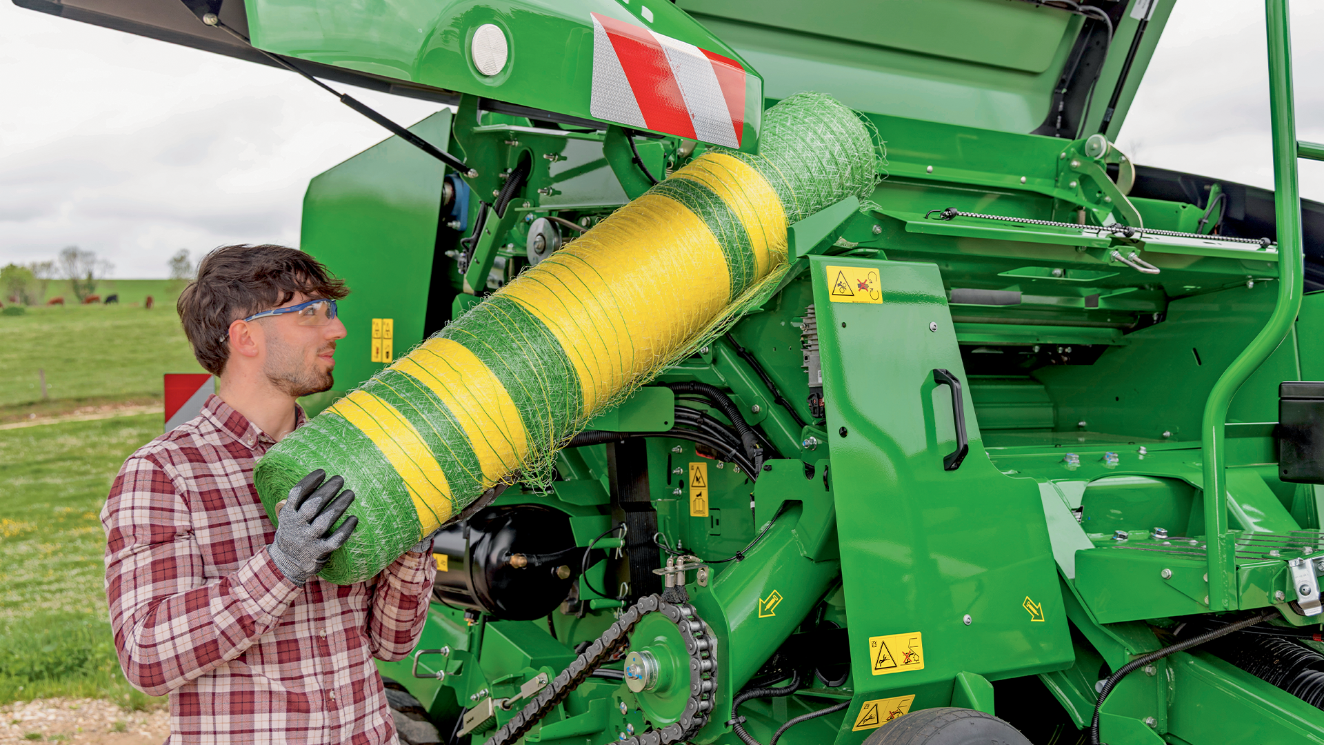 Agriculteur installant un rouleau de filet vert et jaune dans une presse à balles rondes John Deere