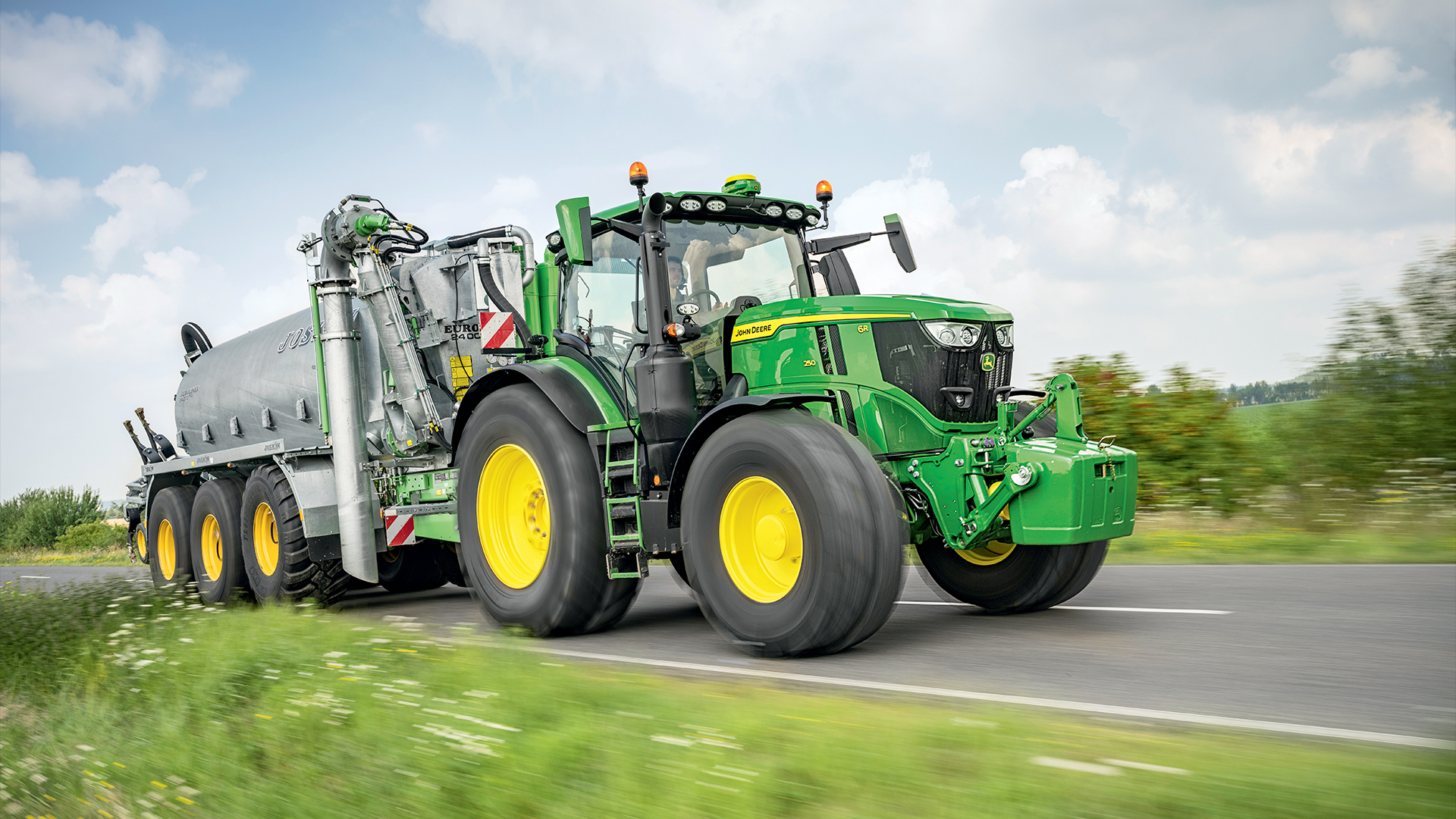 Tracteur John Deere 6R en circulation sur route avec une tonne à lisier.