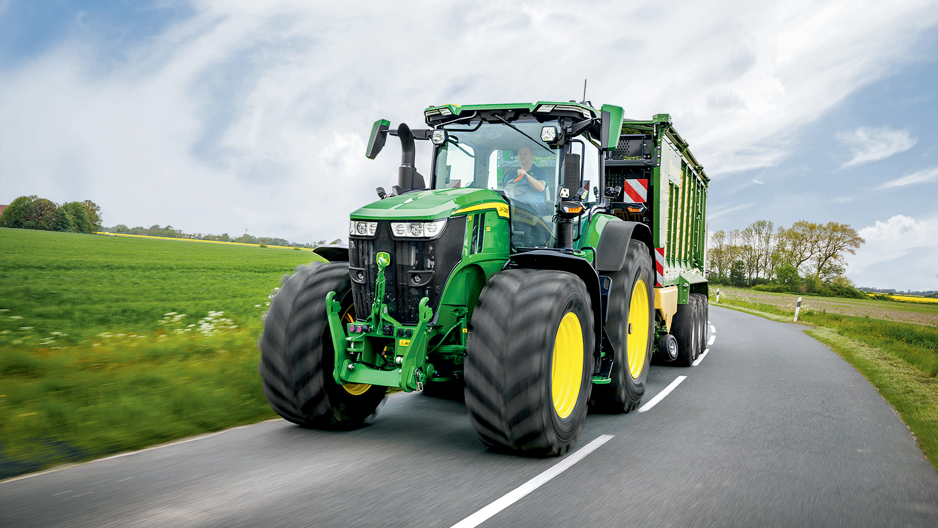 Tracteur John Deere 7R tractant une remorque sur une route de campagne.
